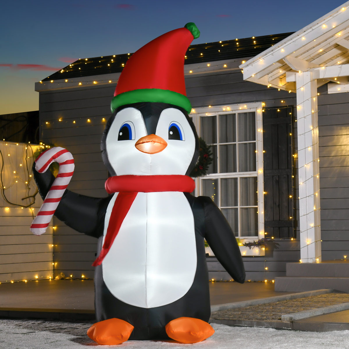 Inflatable penguin with a Santa hat and candy cane in front of a house decorated with lights.