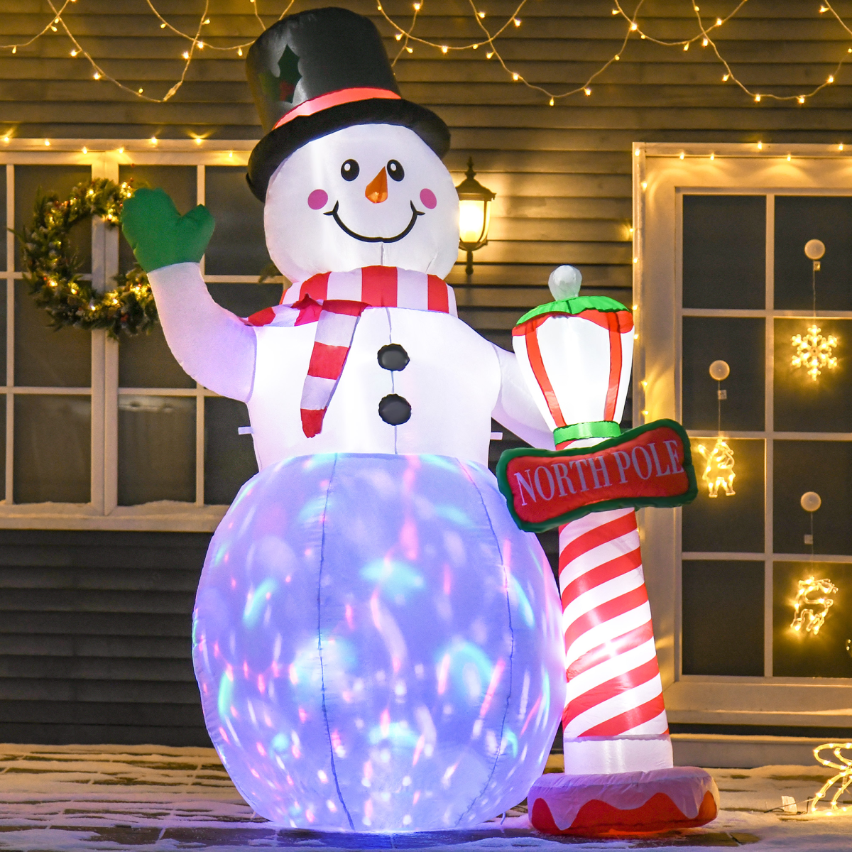Inflatable snowman with a candy cane and 'North Pole' sign in front of a house decorated with lights.