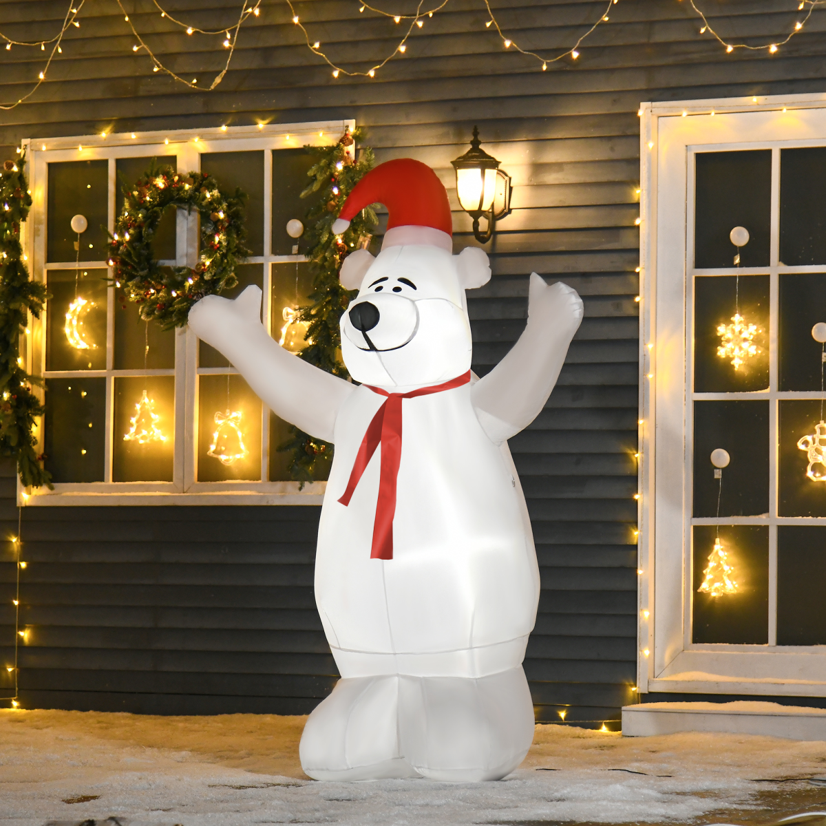 Inflatable polar bear with a Santa hat in front of a house decorated with Christmas lights.