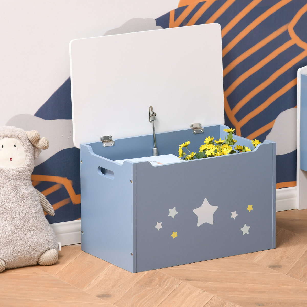 Gray toy box with star designs on a wooden floor, next to a plush sheep toy.