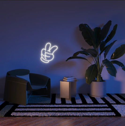 Neon sign of a hand making a peace sign in a dimly lit room with a plant and chair.