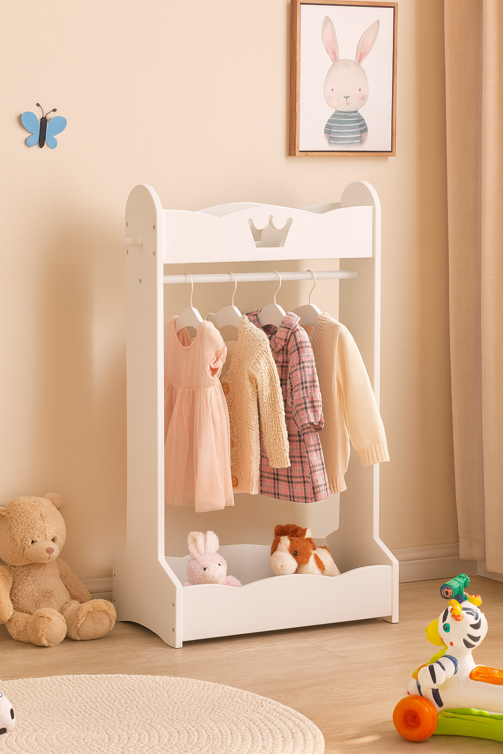 White children's clothing rack with clothes, toys, and a framed picture on a beige wall.