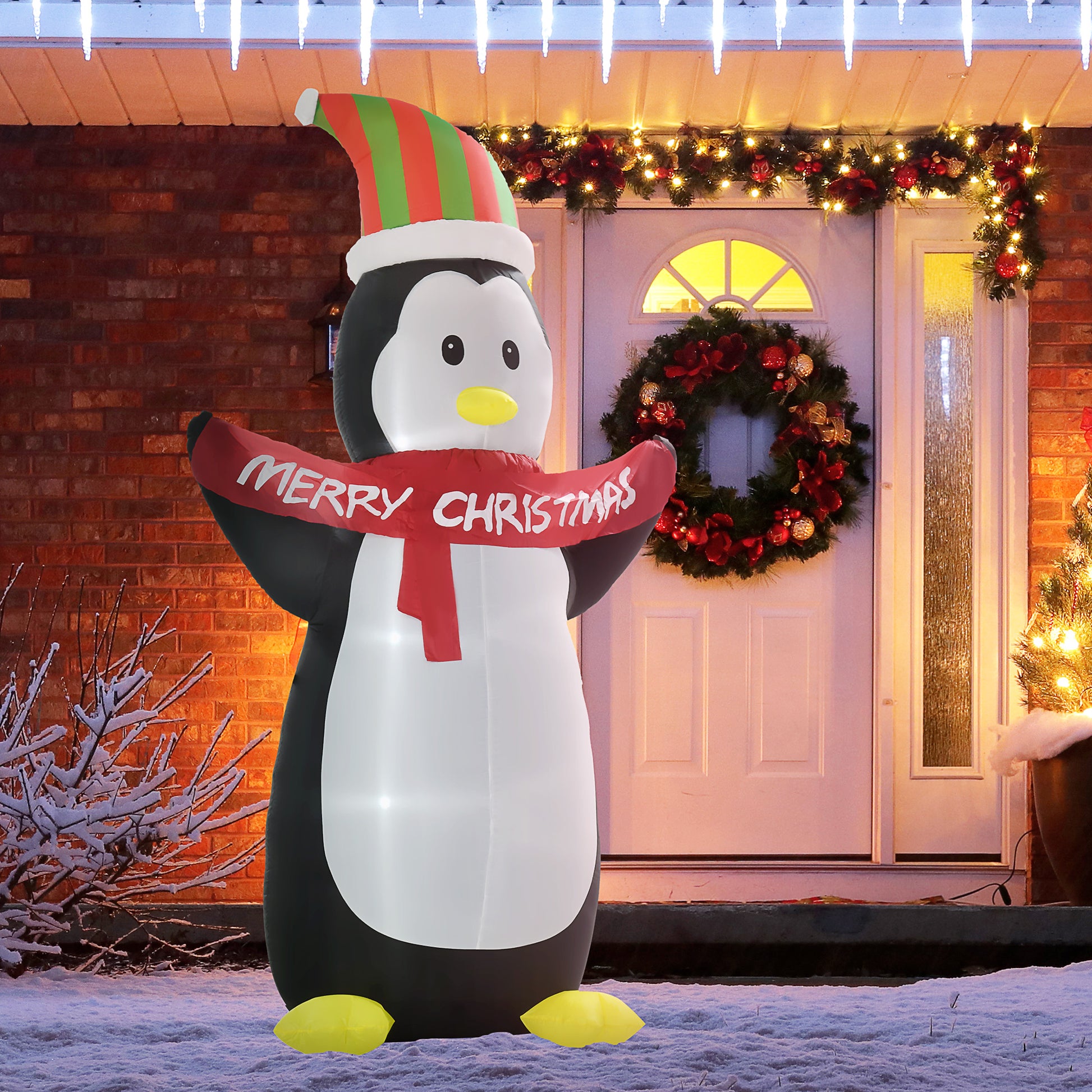 Inflatable penguin with a 'Merry Christmas' scarf in front of a decorated house.